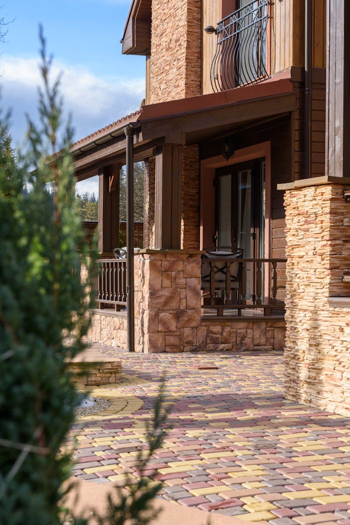 A rustic villa exterior with a sunlit brick pathway and stylish balcony.